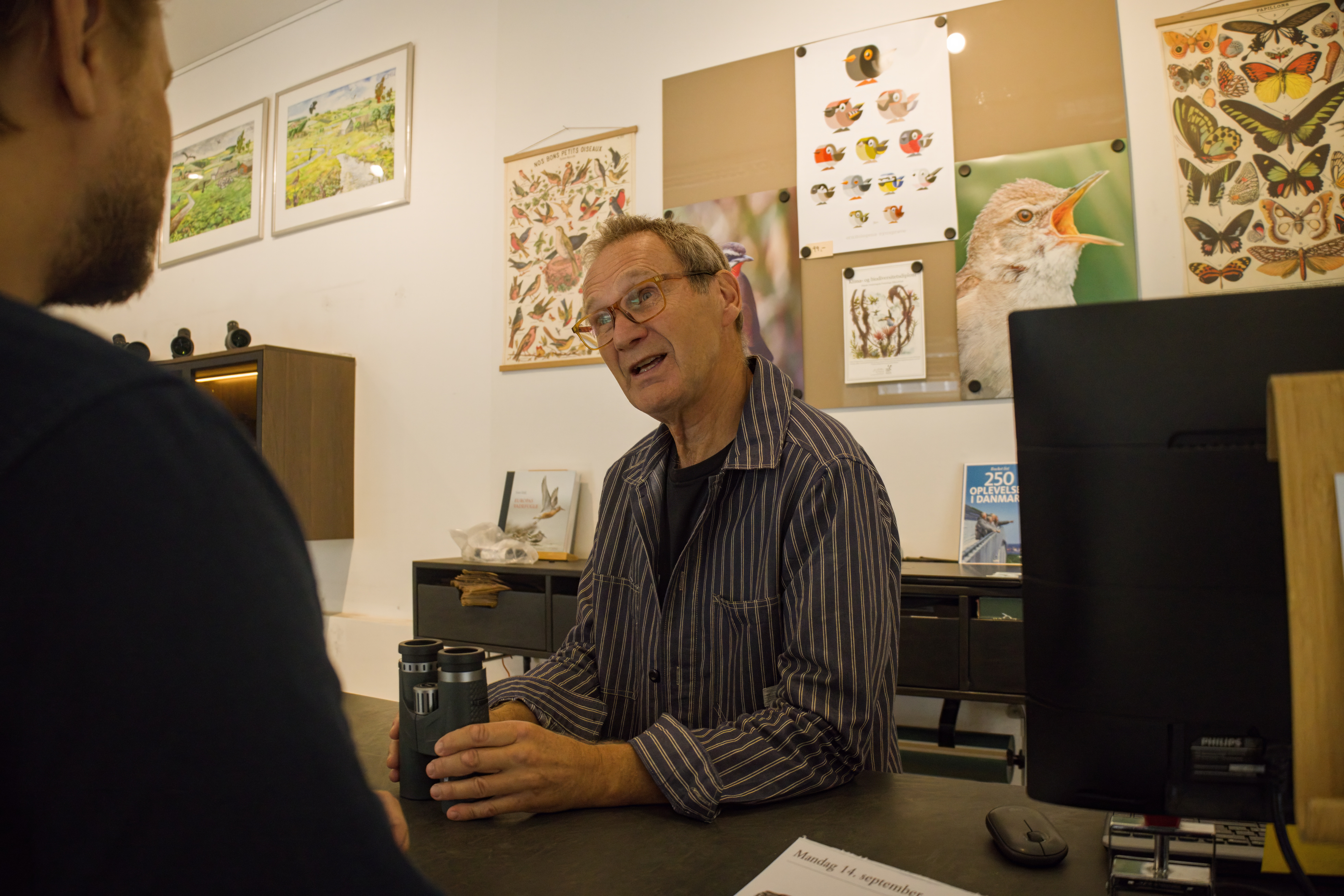 Frivillig i Naturbutikken, Peter Holm, er i færd med at sælge en kikkert til en kunde.